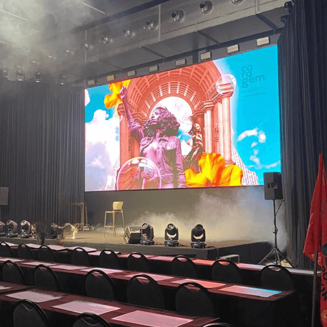 Conference stage with a large screen displaying colorful artwork and empty chairs arranged in rows.